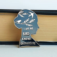Cargar imagen en el visor de la galería, Pin esmaltado de color negro y metal plateado con la inscripción &quot; I am no bird and no net ensnares me&quot; apoyado en libro
